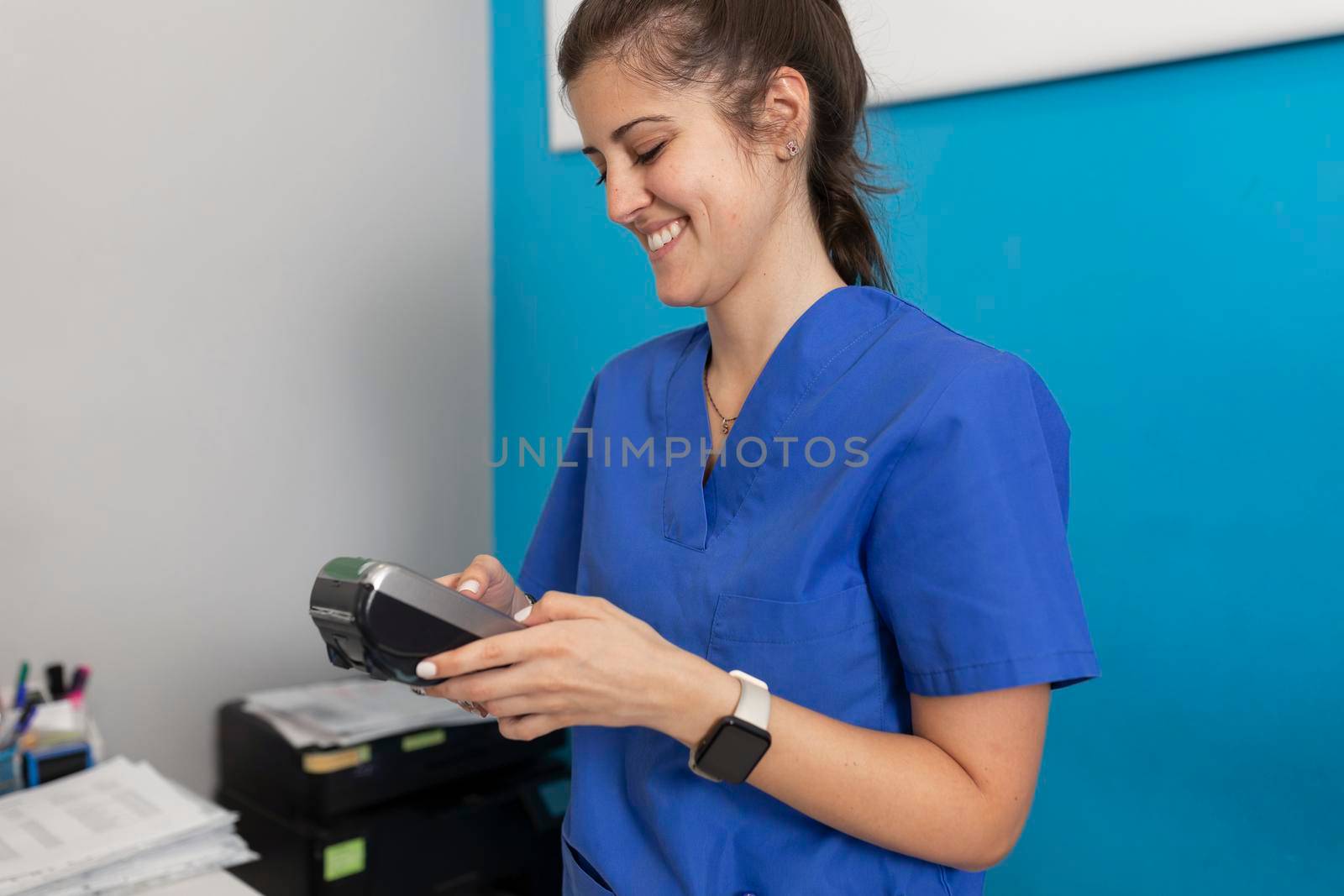 A dental clinic's employee smiles while looking at the dataphone to check if payment, for the services given to a good client has made correctly