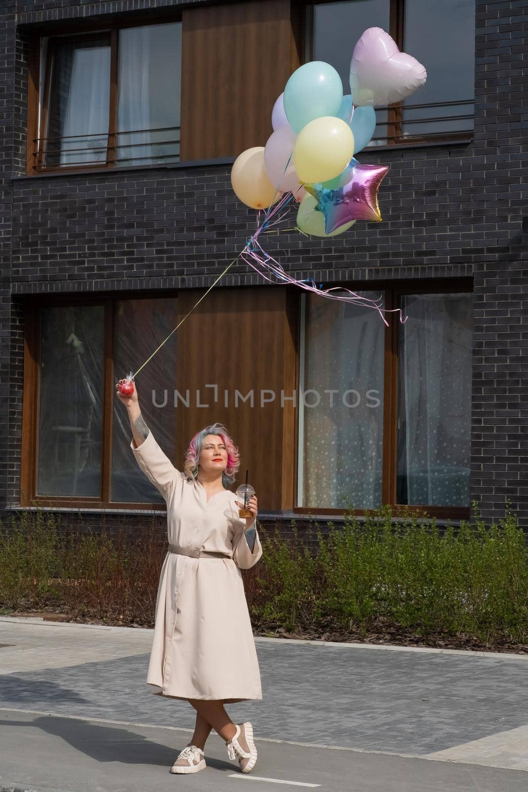 Woman in colored hair walks with an armful of balloons and drinks a refreshing beverage by mrwed54