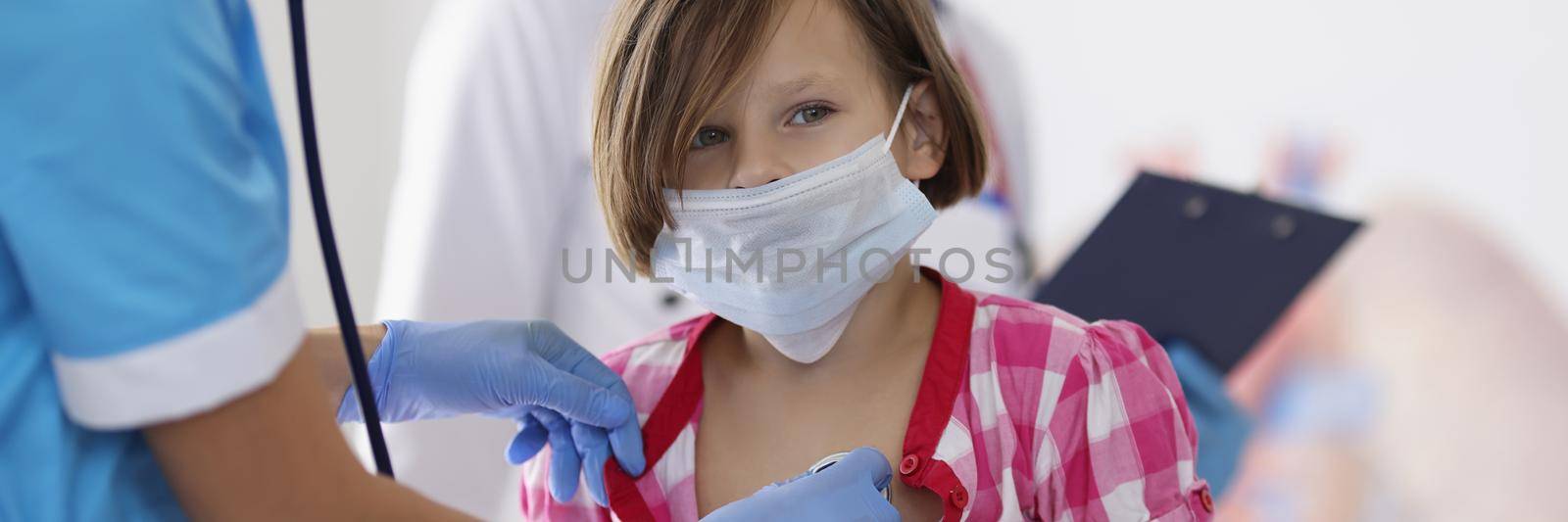 Portrait of girl being examined by pediatrician doctor with stethoscope tool. Calm little girl sit in office and get checkup. Medicine, appointment concept