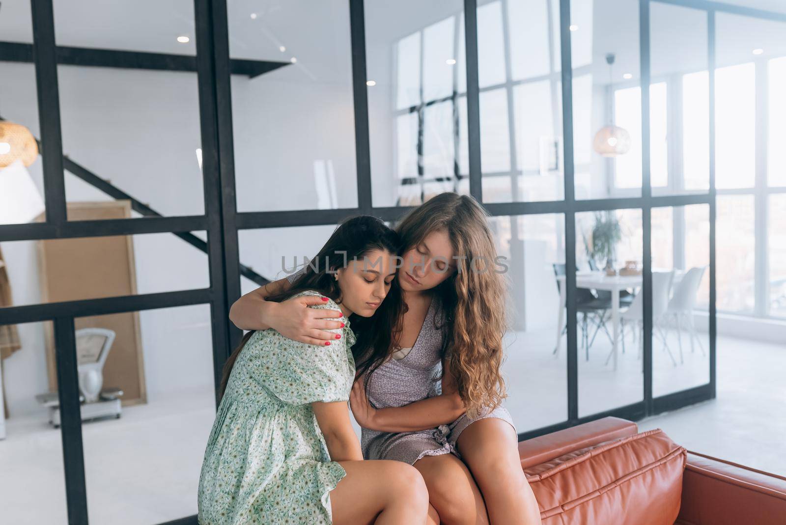 Two young attractive women sit on a sofa in the room and talk about something.