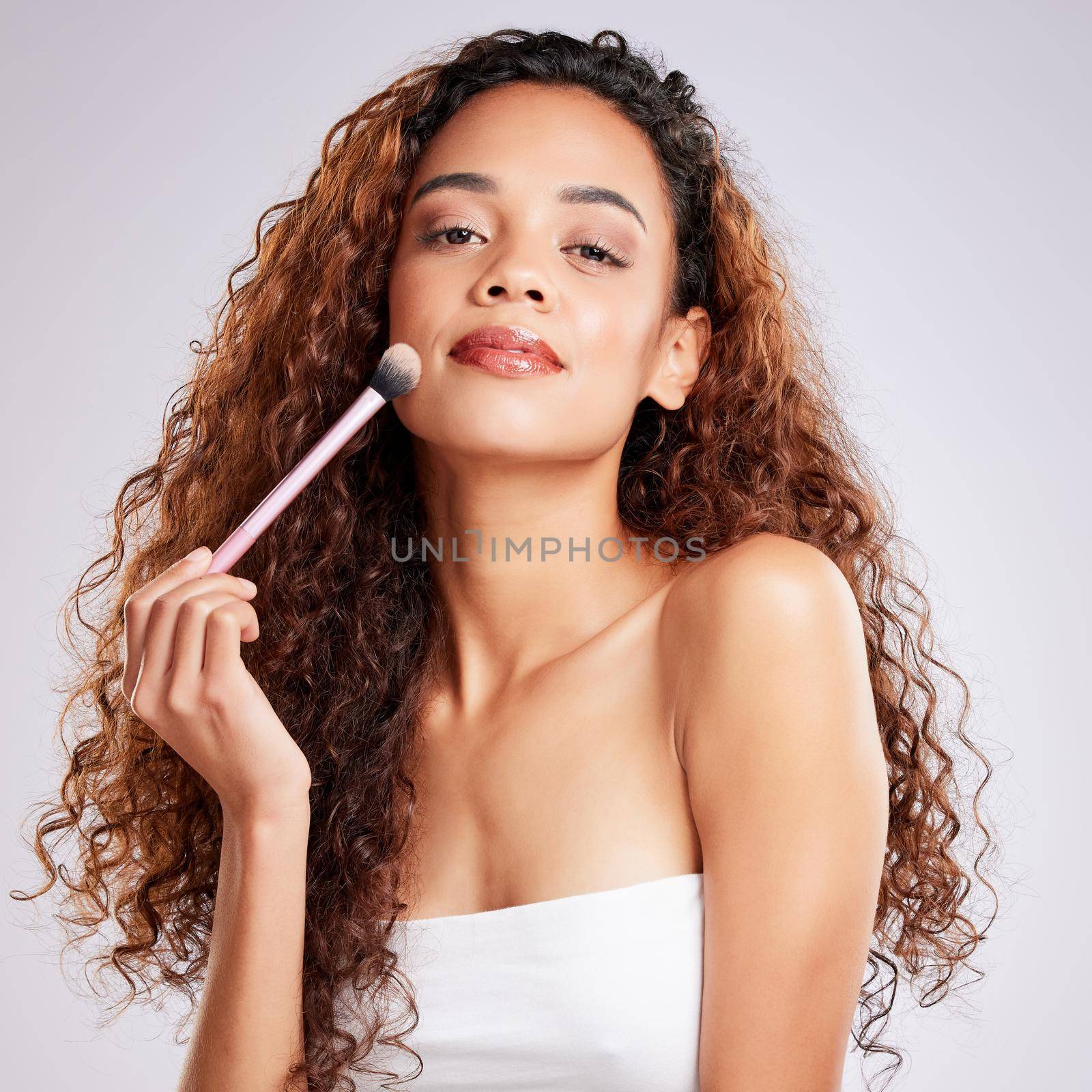 a young woman applying makeup against a grey background.