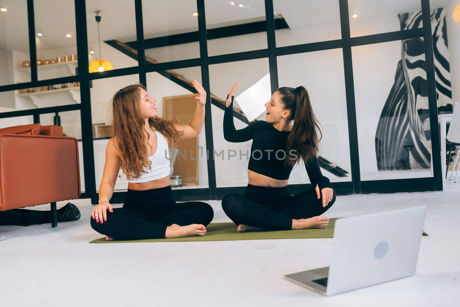 Two women while sitting in the lotus position give a high five by teksomolika