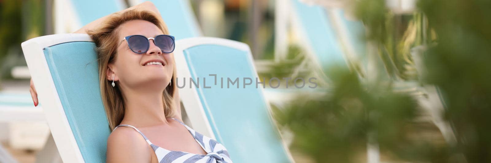 Happy young woman on sit on sunbed in pretty summer dress. by kuprevich