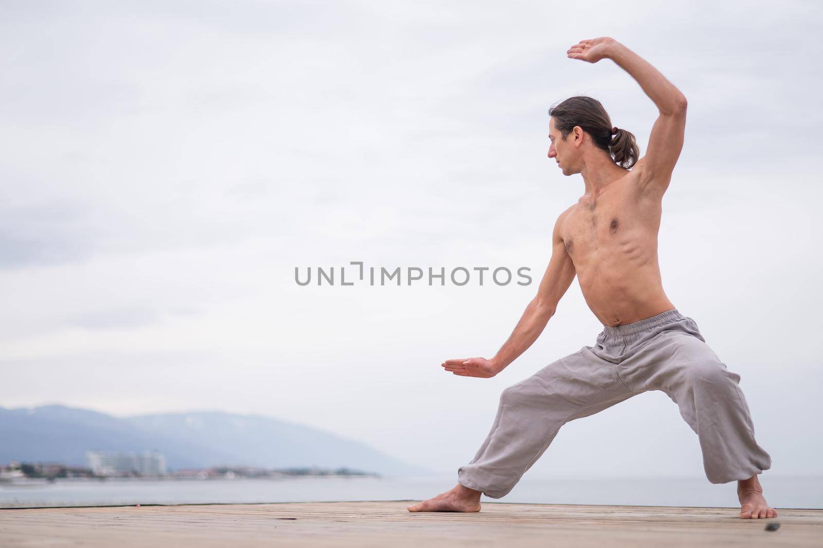 Caucasian man with naked torso practicing wushu on the seashore. by mrwed54