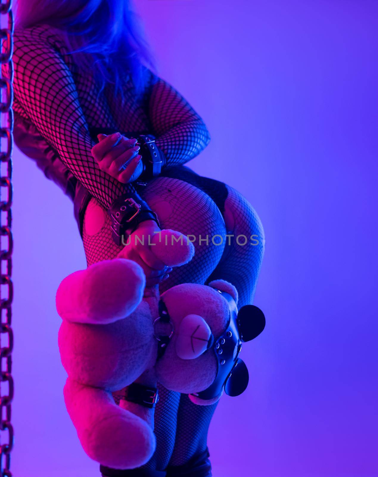 the buttocks of a sexy girl in leather bdsm handcuffs and a teddy bear in a mask and party dresses