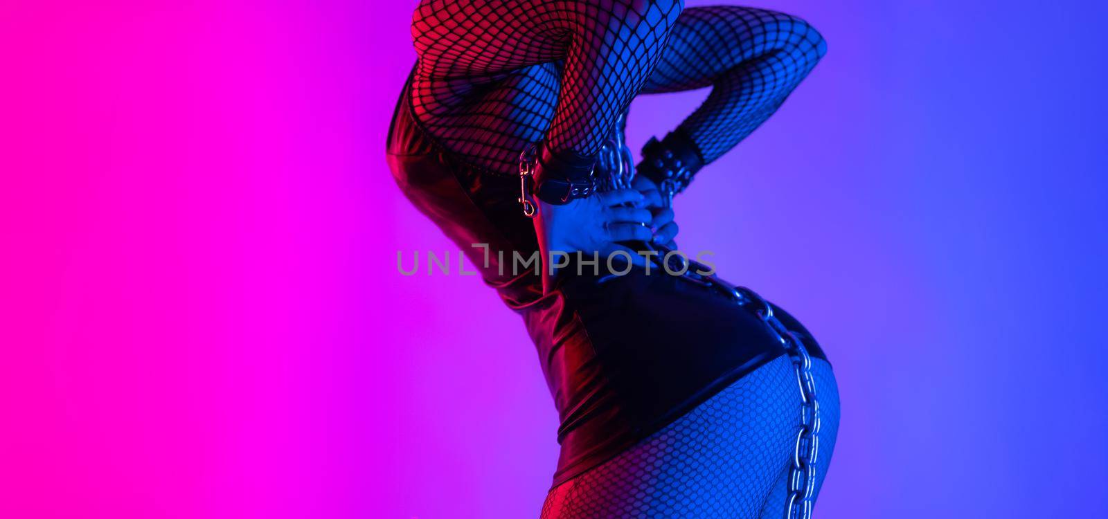 the sexy buttocks close-up of a girl in a latex bdsm mistress costume with torn tights in neon light