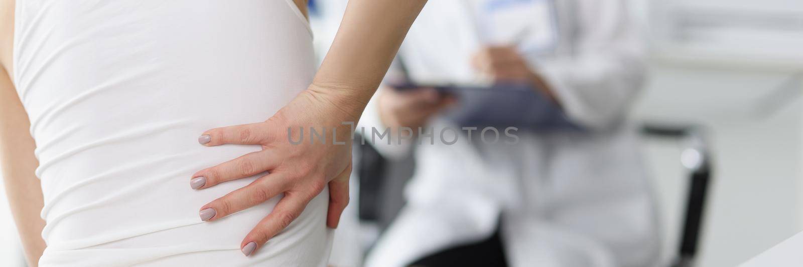 Close-up of female patient complain on back pain and touch side of body. Doctor listen to client and propose diagnostic. Healthcare, trauma surgeon concept