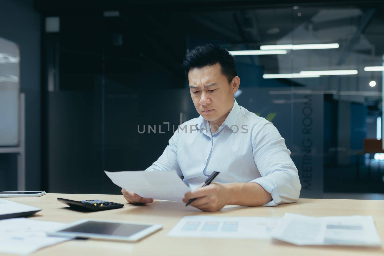 Upset and unhappy asian businessman reading documents and letter from bank, businessman at work in office disappointed with work result