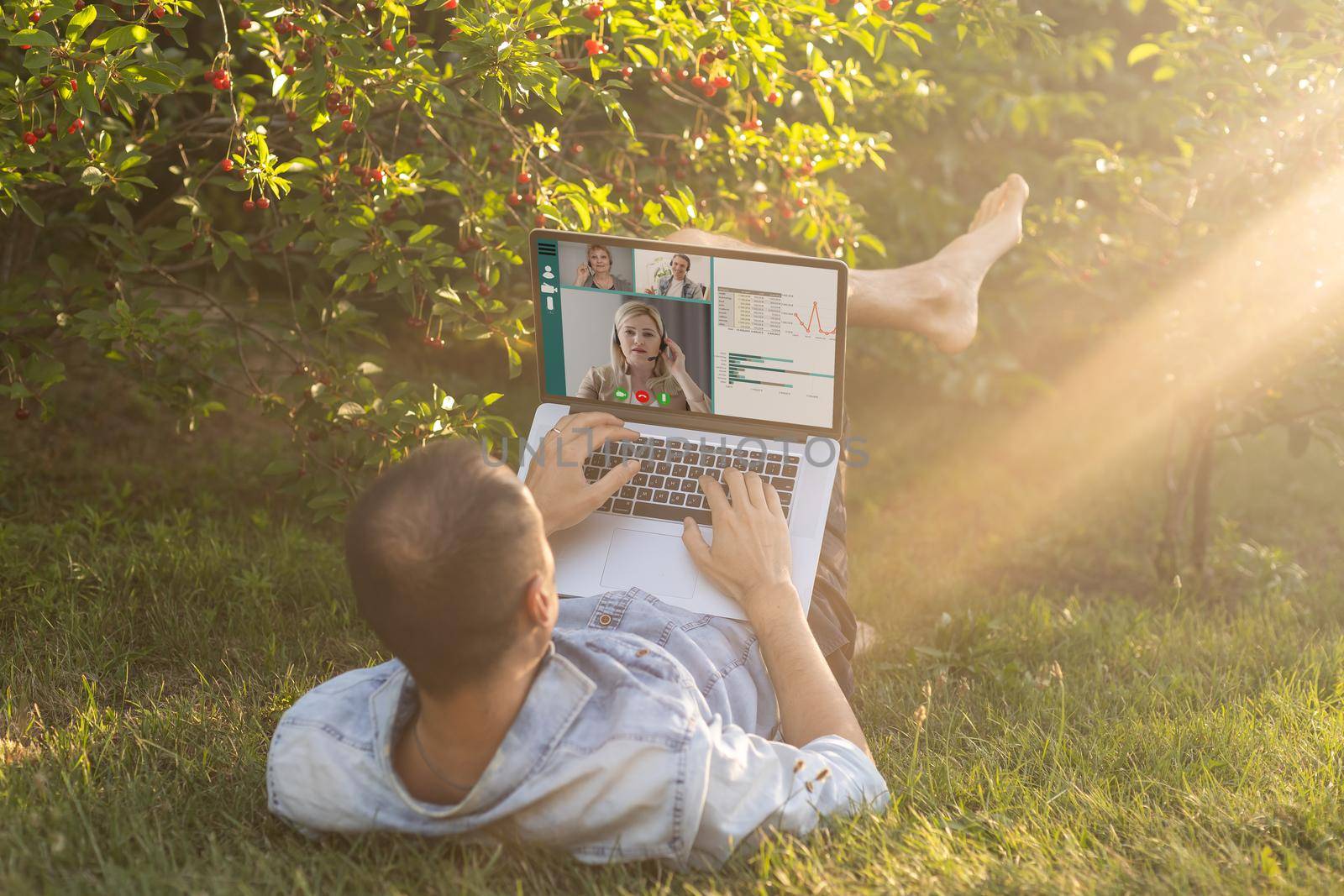 Young man in the garden in summer on the laptop computer while chatting online as a freelancer