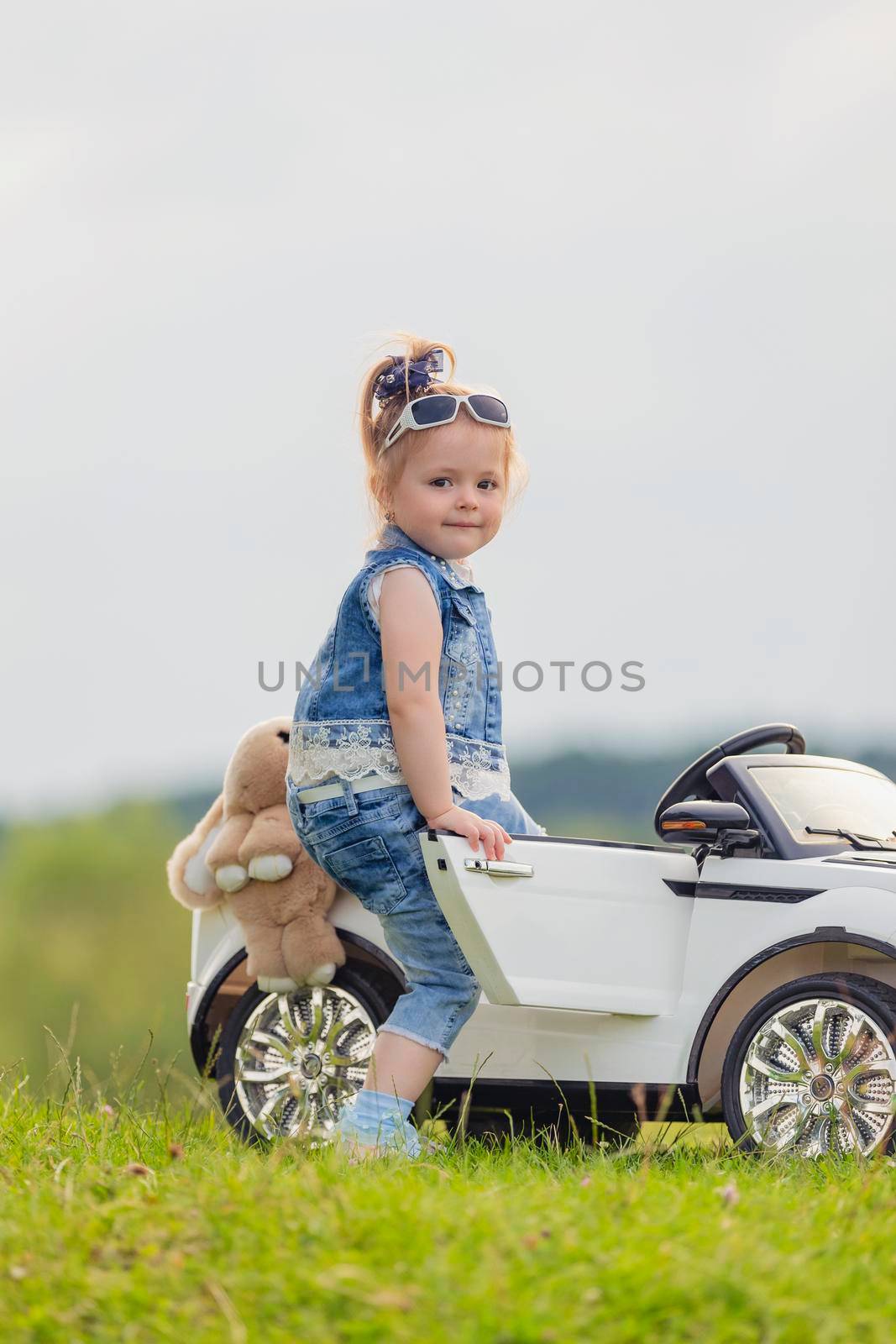 small child stands near his car on the lawn