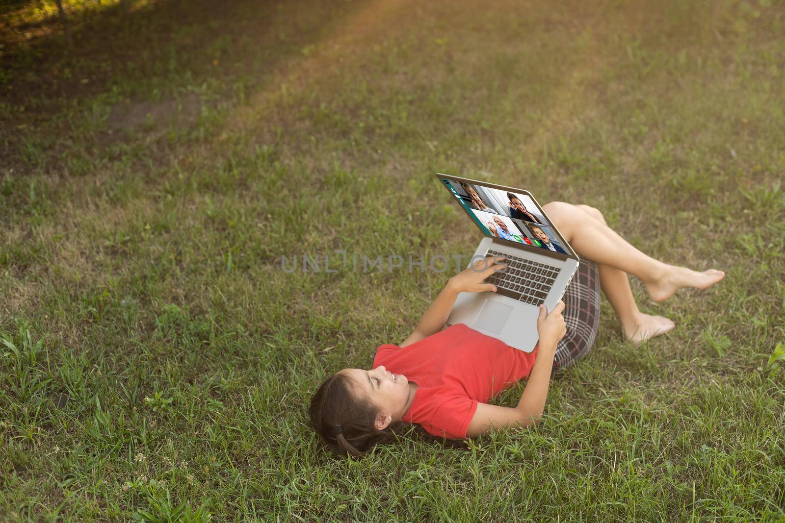 Beautiful young lady is chatting with friends outdoors as it is very useful to be in nature. Laptop is the best friend for a child nowadays. Green and vast meadow by Andelov13