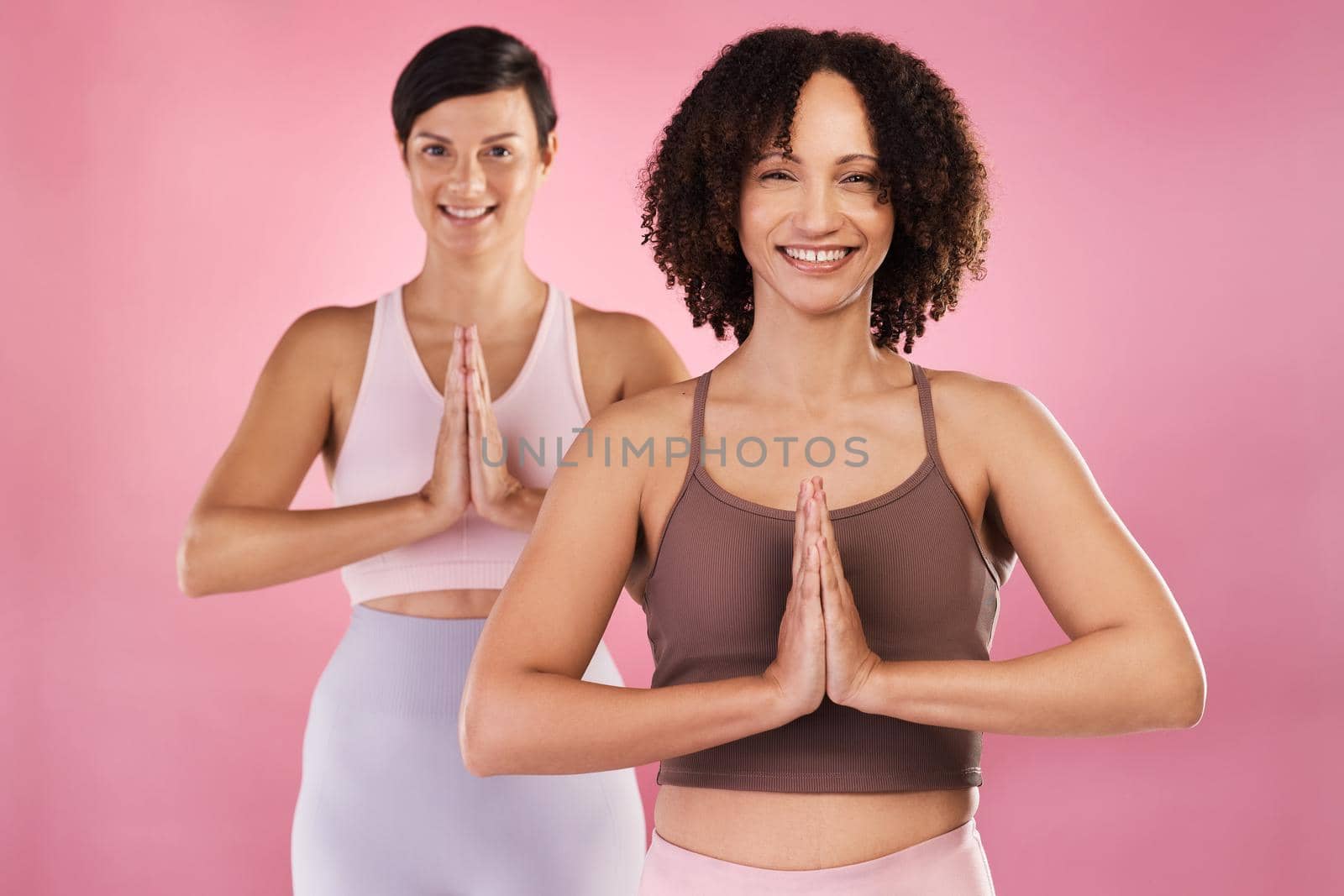 Cropped portrait of two attractive young female athletes meditating in studio against a pink background.