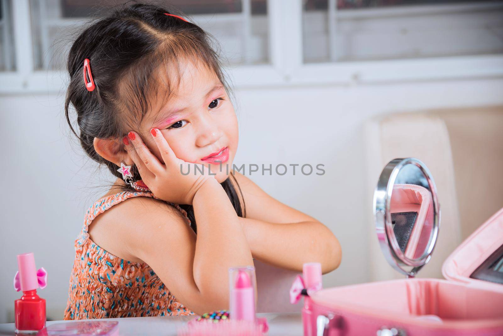 Closeup of happy kid is beautiful make up face with cosmetics toy, Asian adorable funny little girl making makeup her face, Learning activity to be woman, fashion beauty children at home