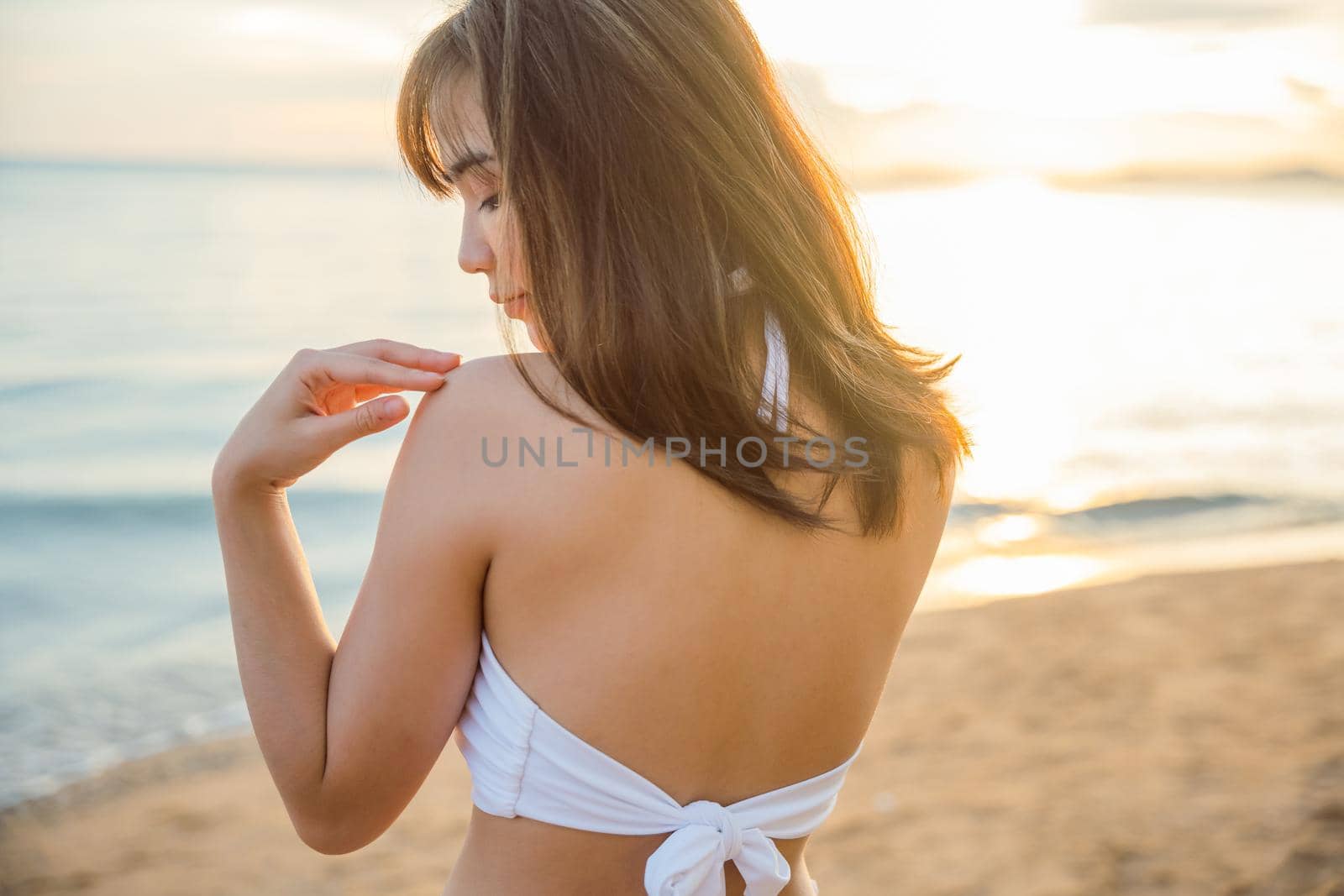 Portrait of young woman in white bikini swimsuit standing posing and holding sunglasses on tropical beach, Happy beautiful Asian girl in swimwear on summer holiday travel