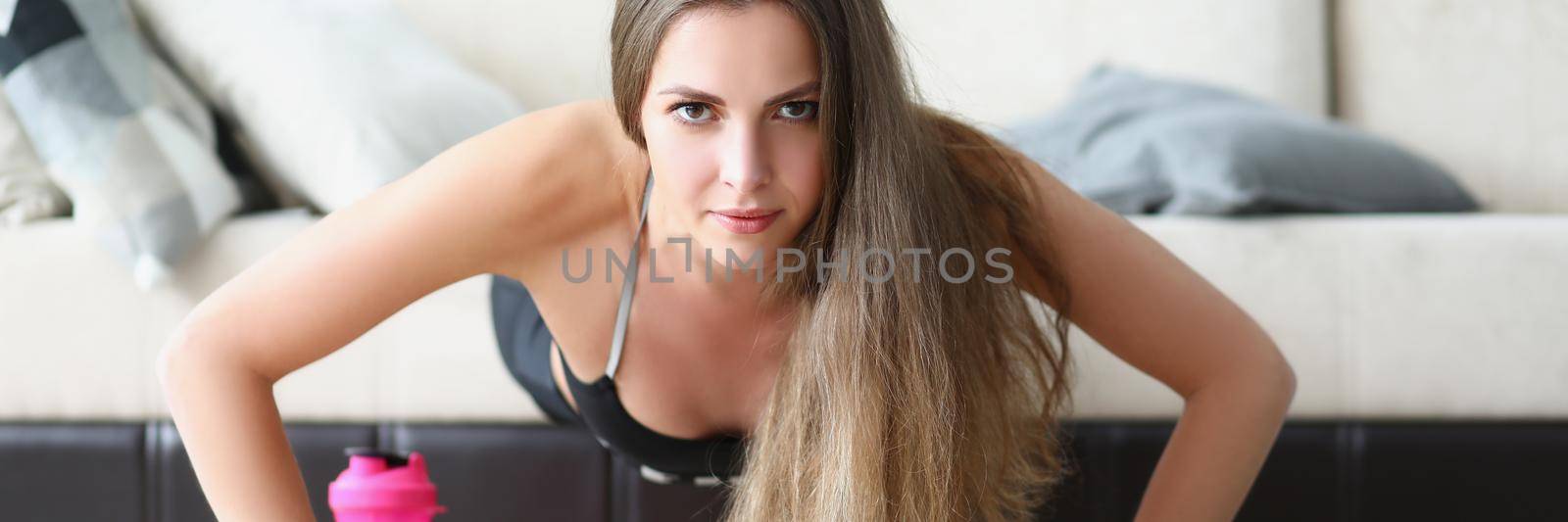 Low angle of sweaty young woman performing exercise on floor in living room. Concentrated girl train body with equipment at home. Sport, health concept