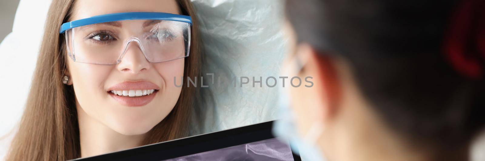 Portrait of patient on dental consultation in clinic, doctor examine teeth x ray on digital tablet device. Stomatologist on appointment. Teethcare concept