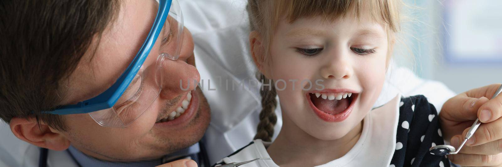 Man pediatrician check little girls health condition using special tool for mouth by kuprevich