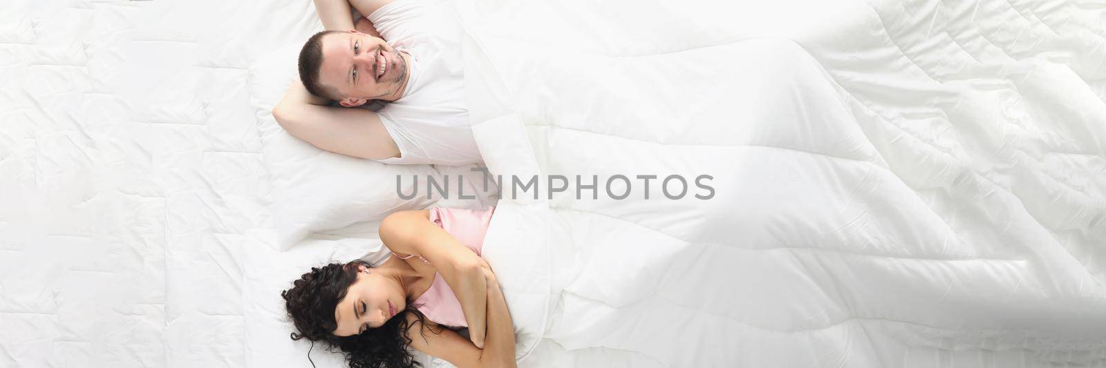 Top view of wife and husband happily laying bed, white bedclothes. Wake up and start new day, good morning. Comfort, relaxation, family, sweet home concept