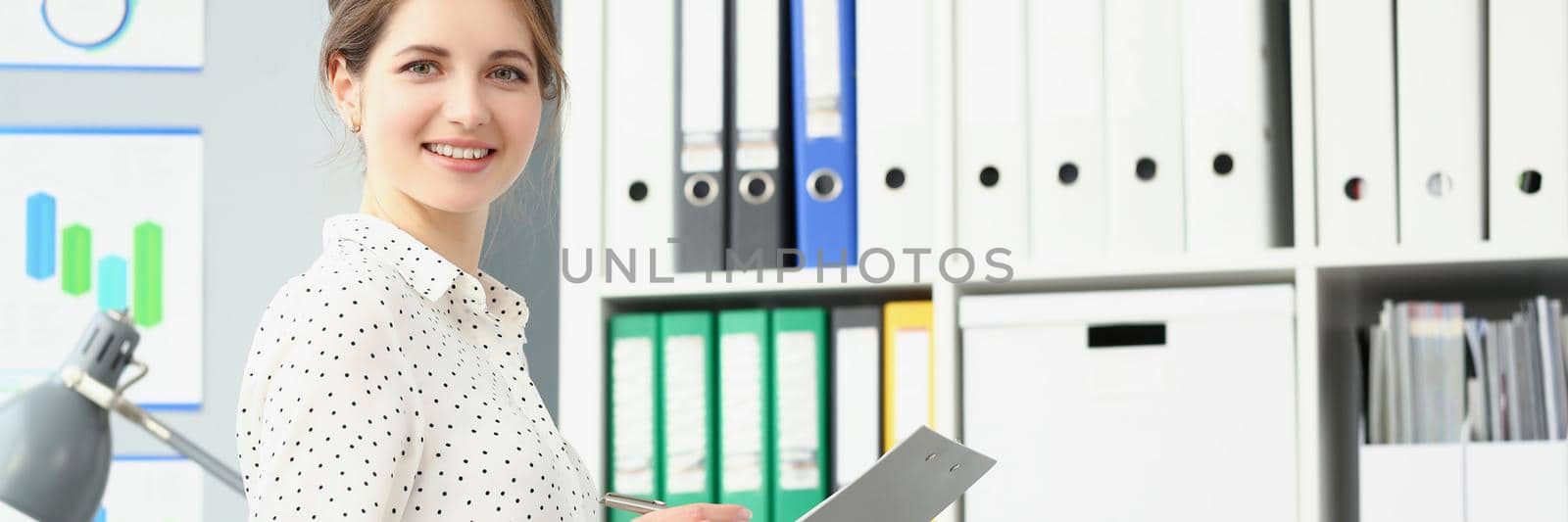 Portrait of smiling employee woman posing in conference room, making notes on paper. Businesswoman report on business meeting in company. Biz firm concept