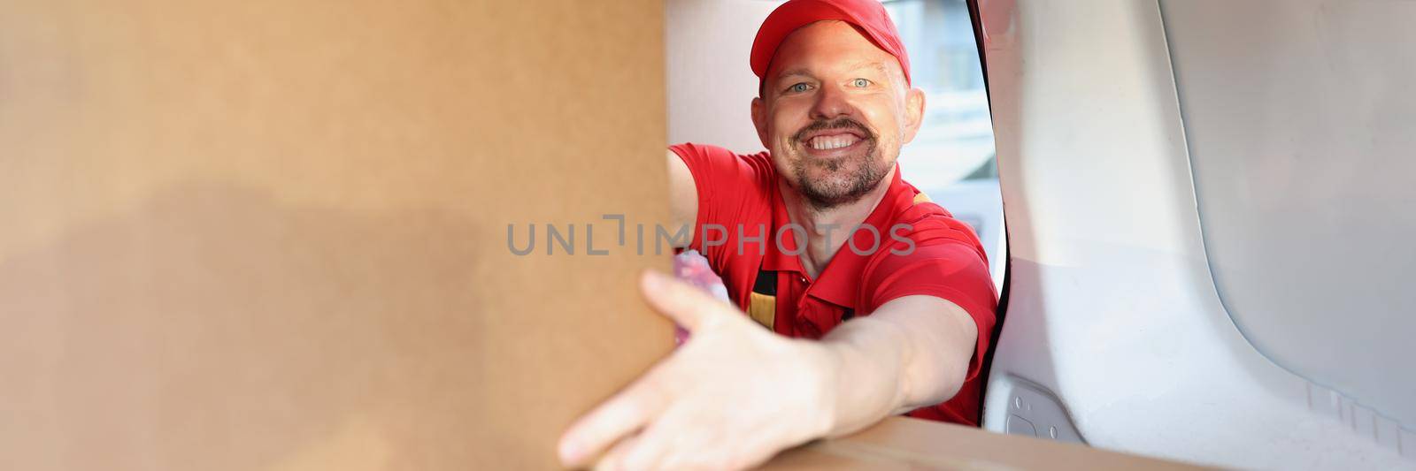 Portrait of man enjoying working in delivery company, put boxes in truck for further delivery on address. Happy man help with relocation. Handyman concept