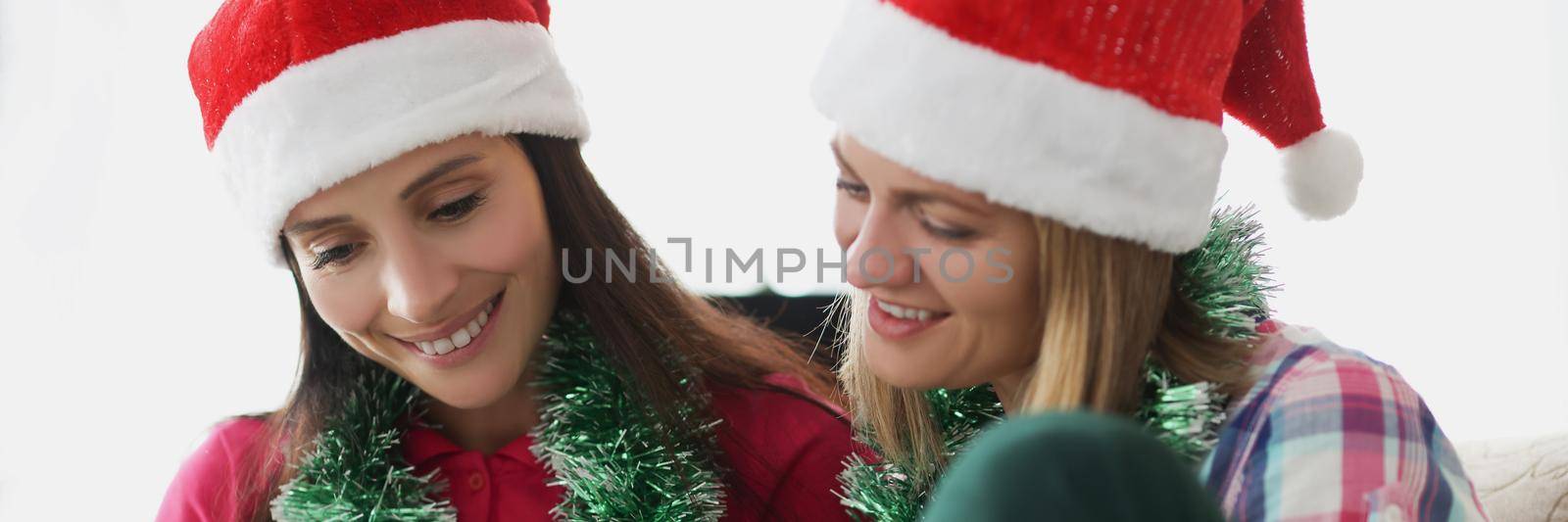 Portrait of girls write down plans or wishes for presents to get on new year. Friends in festive hats sit on sofa and plan. Christmas, make wish concept