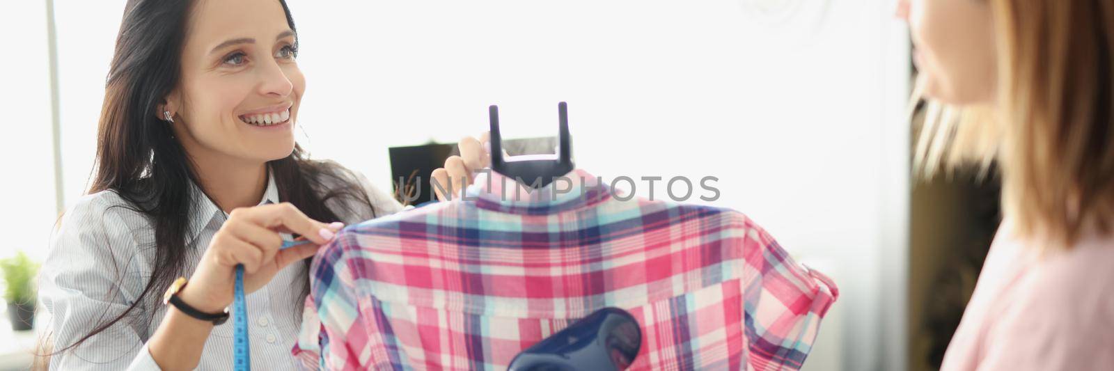 Girls atelier coworkers use clothing steamer on shirt, prepare for selling by kuprevich