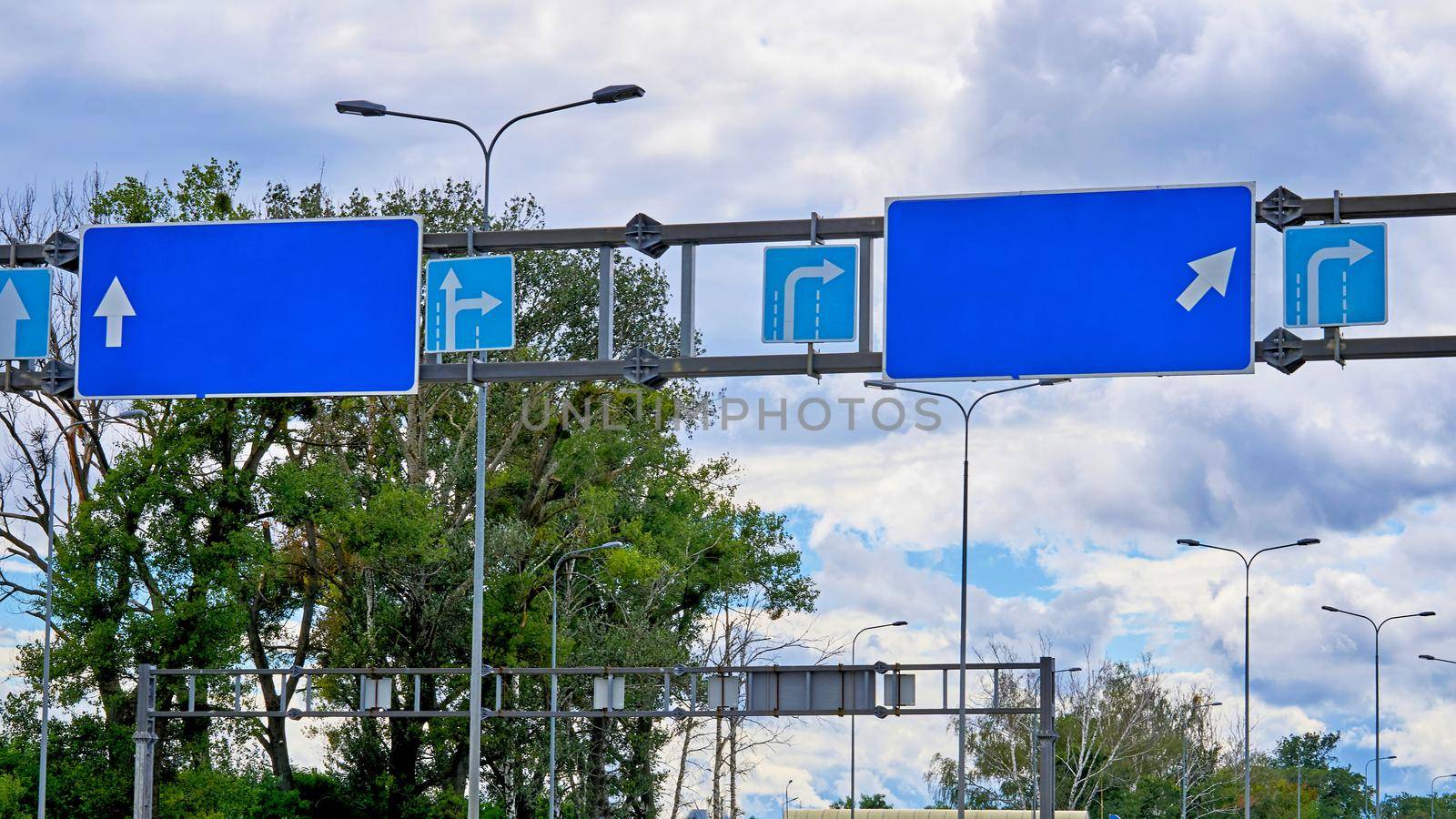 Blue pointing empty road signs with arrows and cloudy sky and trees by jovani68