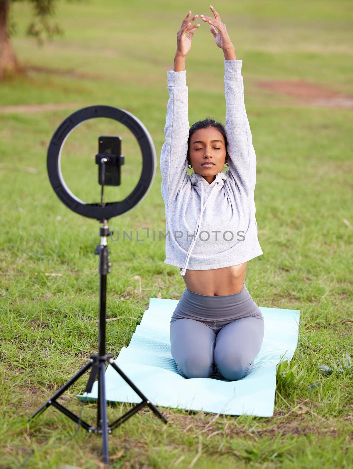 a young woman recording herself doing yoga in the park.