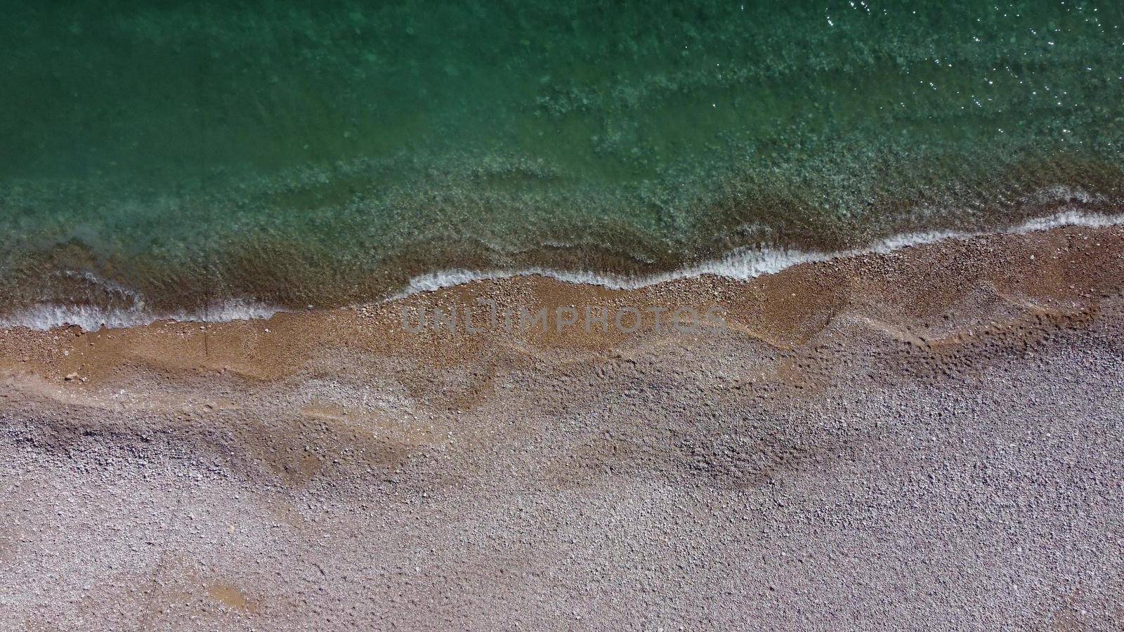 Aerial view from above on azure sea and pink pebbles beach. Small waves on cristal clear water surface in motion blur. Summer ocean sea beach background. Nobody. Holiday, vacation and travel concept by panophotograph
