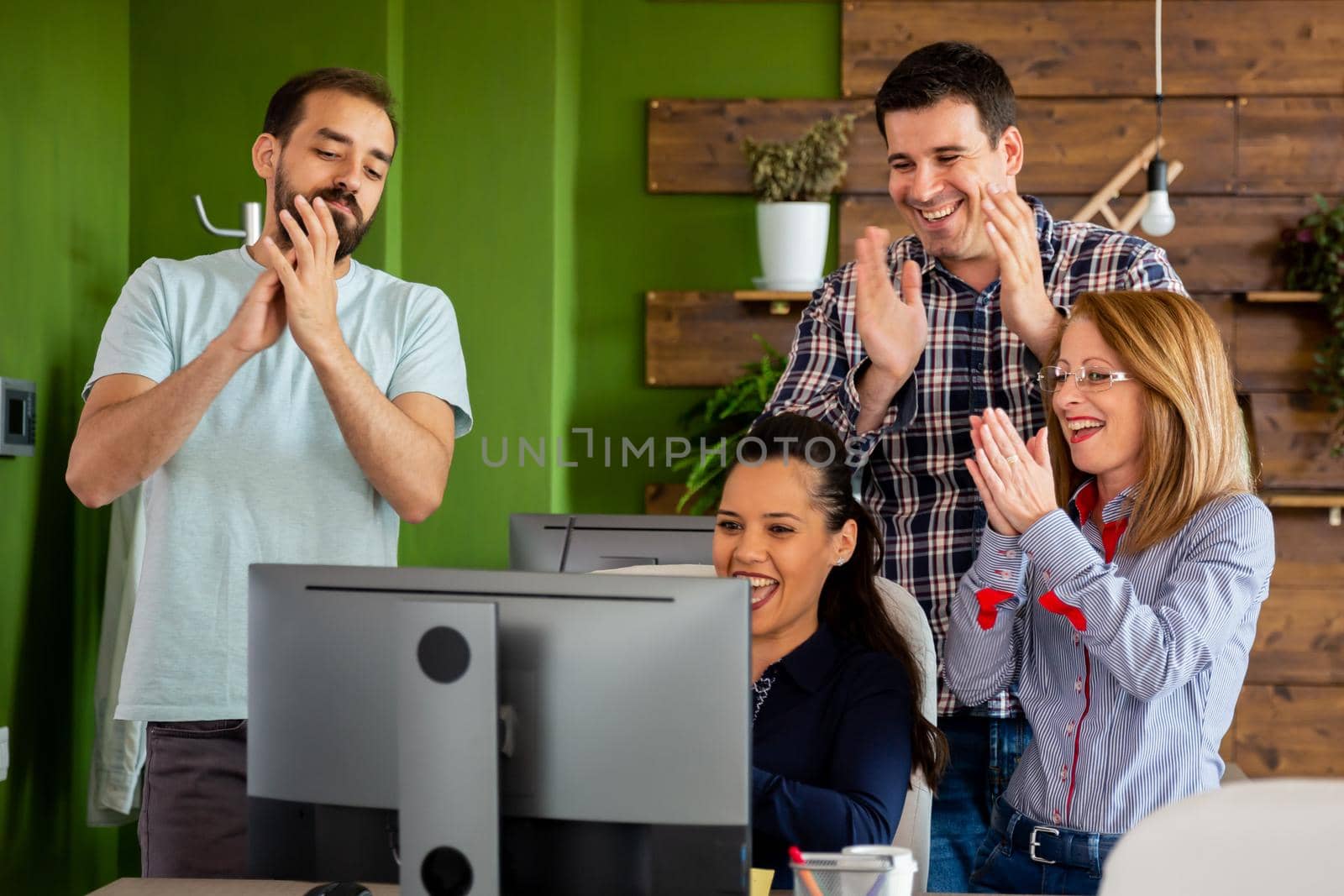 Young creative team in start-up company clapping in front of PC screen. Happy news and big contract