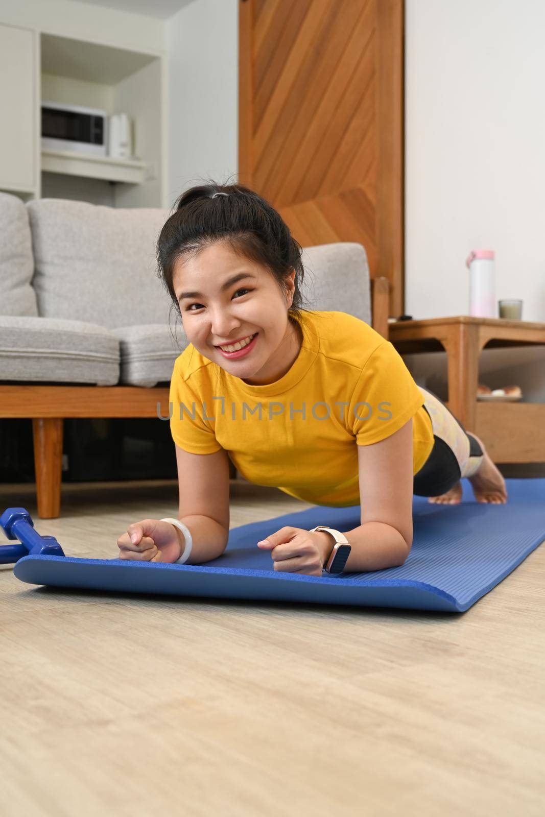 Sporty young woman doing plank on mat in living room. Fitness, sport and healthy lifestyle concept by prathanchorruangsak