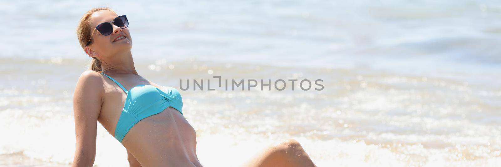 Portrait of beautiful young woman posing in swimsuit on sand under hot summer sun. Female get tan on holiday, resting alone. Trip, modeling, sea concept