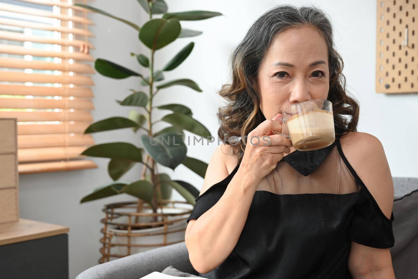 Serene middle aged woman drinking hot coffee, relaxing on couch at home. Stress free, positive mood concept.