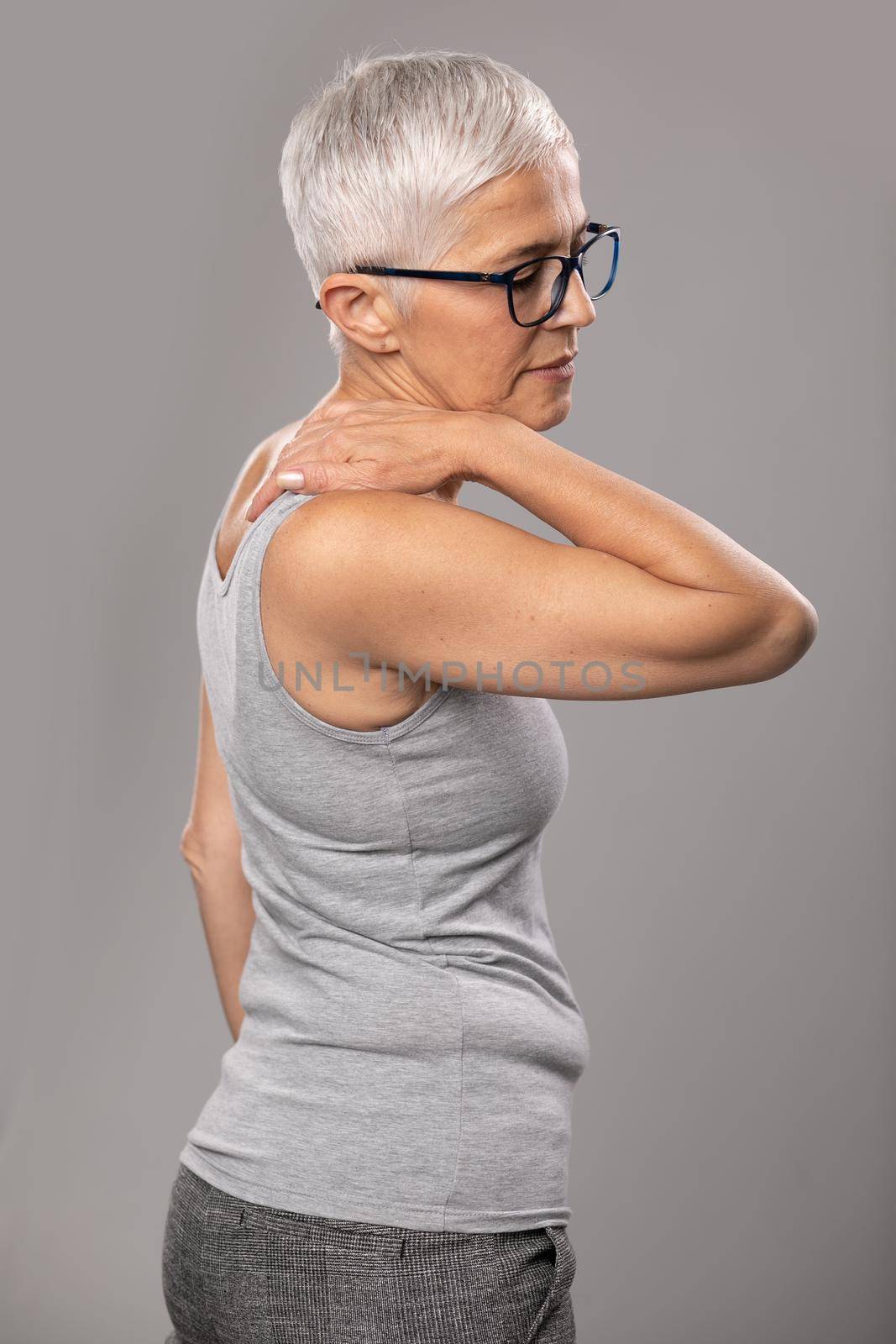 Backache pain in back, senior old woman with short gray hair and glasses show body and spinal muscle problems by adamr