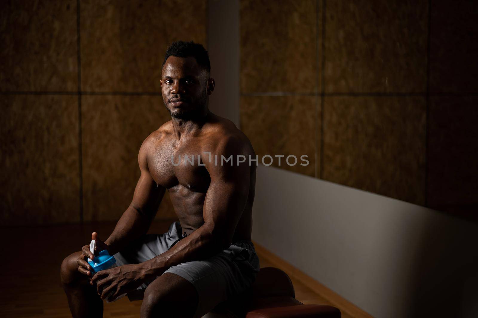 Shirtless african american man drinking from a shaker in the gym