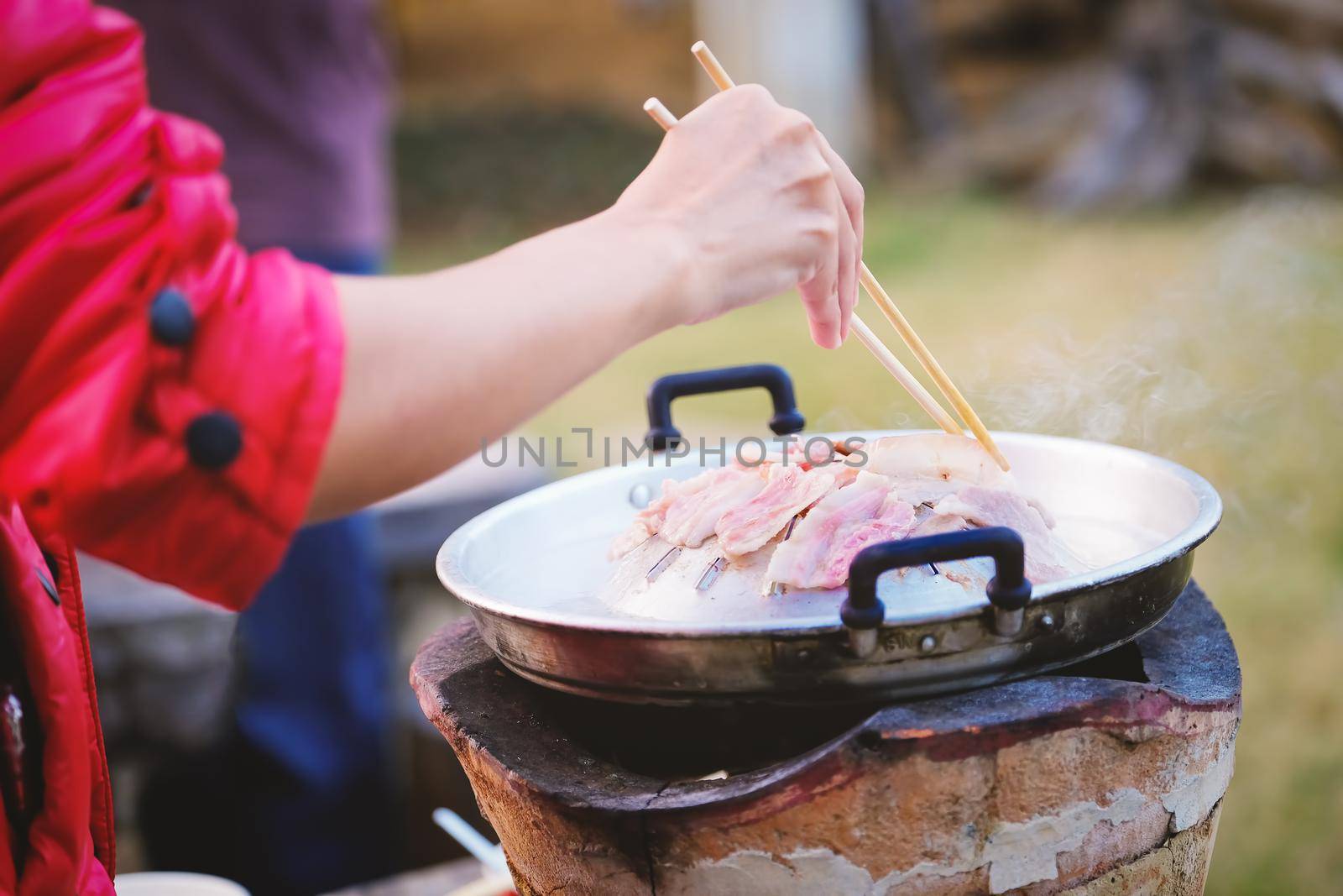 Focus on the pork belly, woman is using chopsticks to hold the pork on the pan. by Manastrong