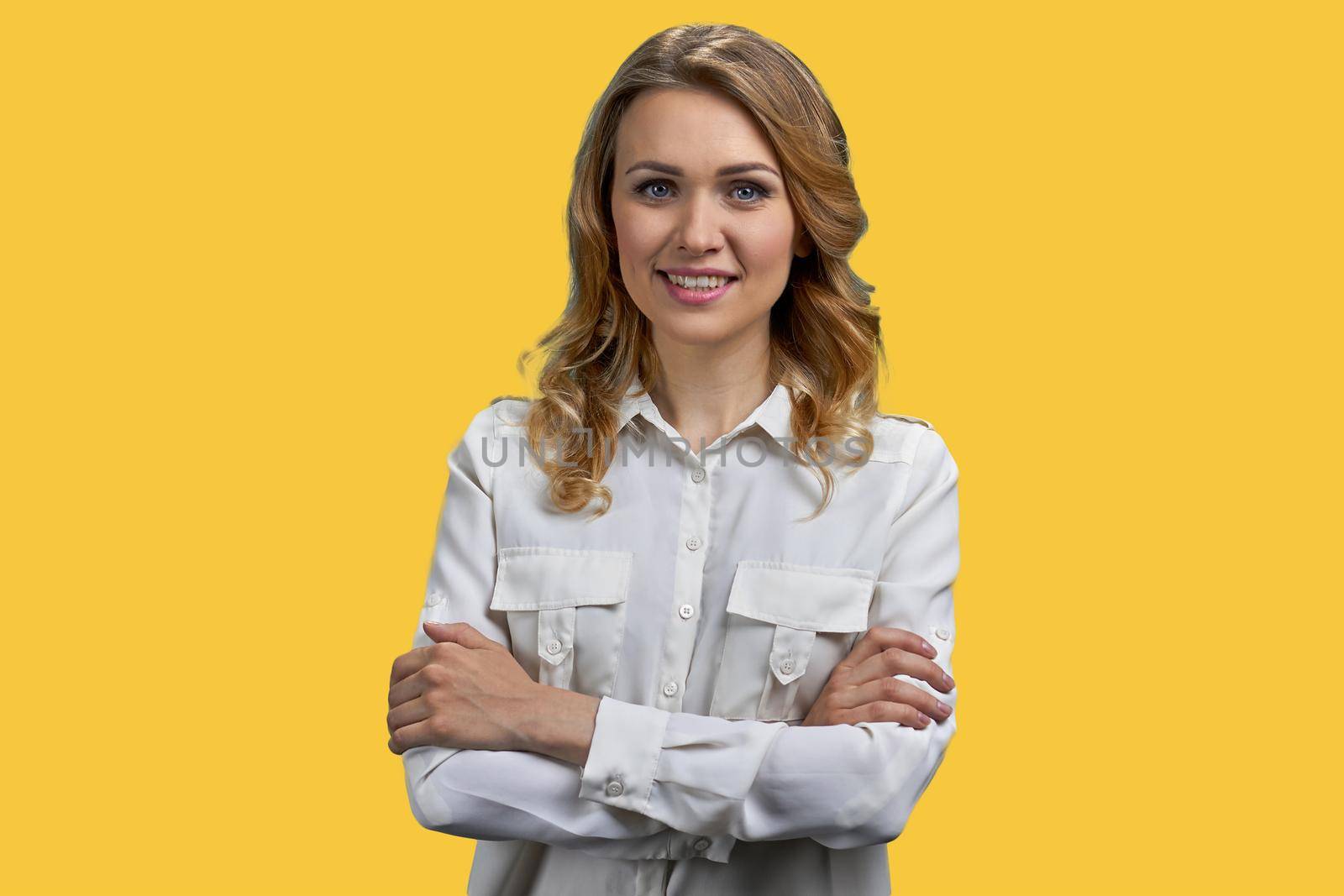 Young pretty business lady looking at camera with crossed arms. Portrait of beautiful smiling woman on yellow background.