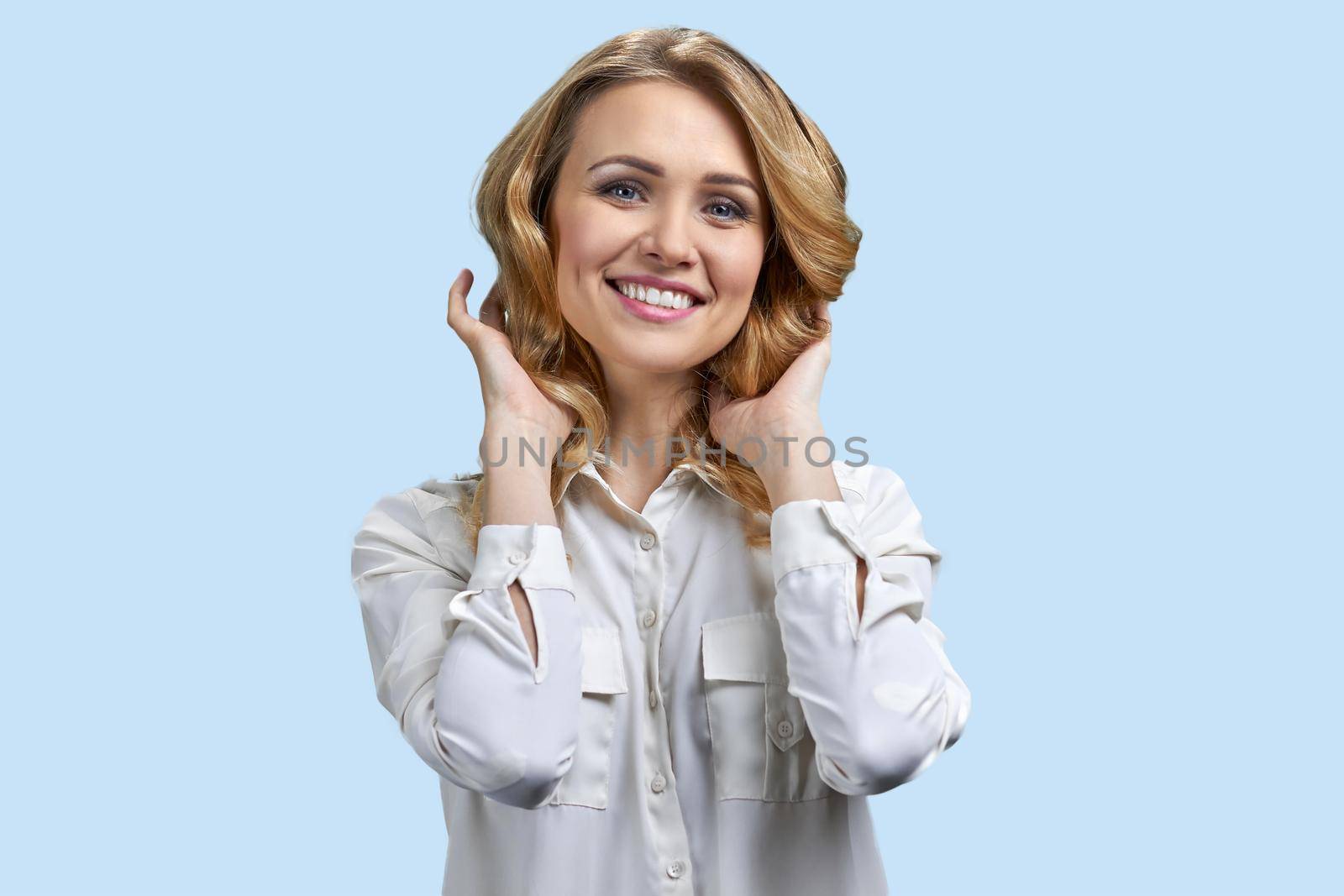 Portrait of beautiful young woman touching her hair and smiling. Happy caucasian woman posing at camera on blue background.