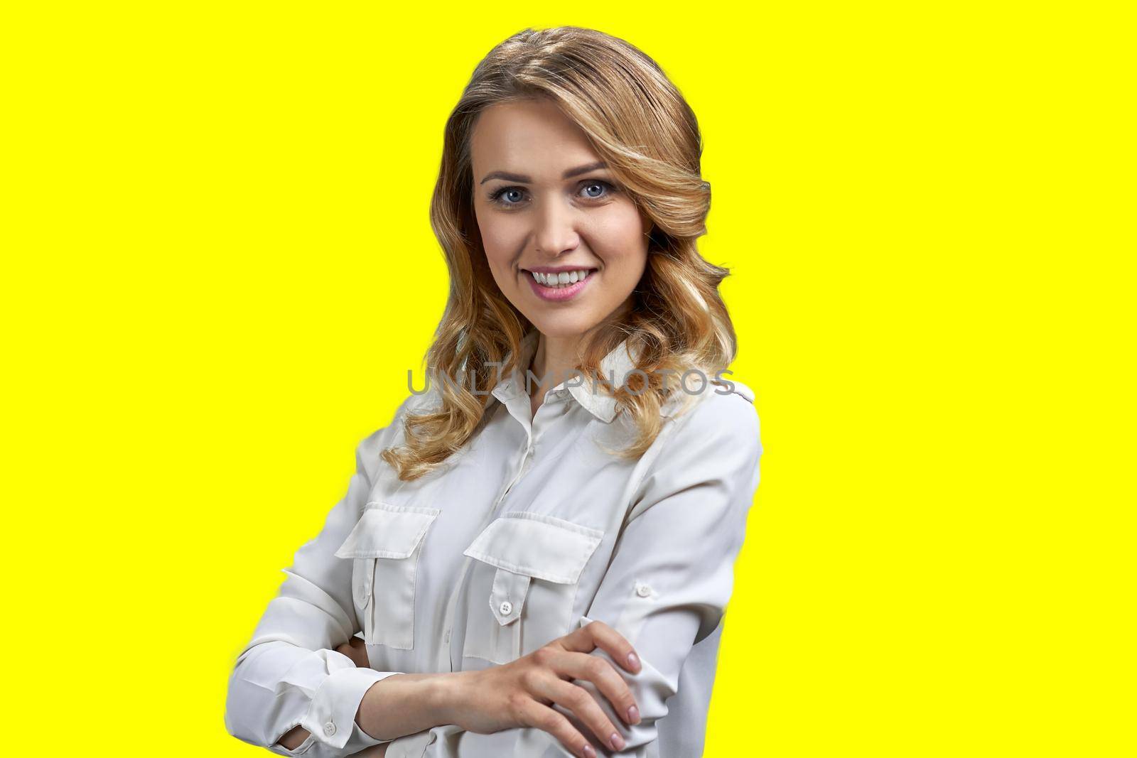 Beautiful young woman in white blouse looking at camera with crossed arms. Pretty girl posing at camera on yellow background.