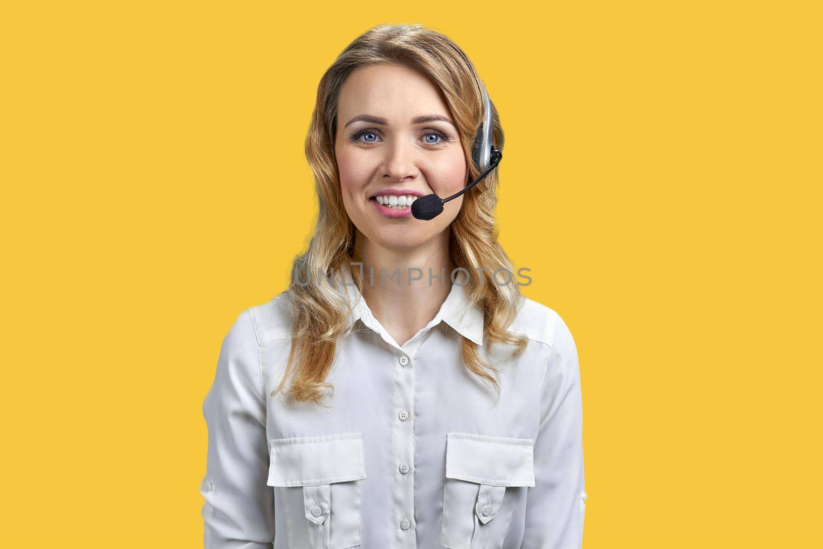 Portrait of beautiful call center agent looking at camera against color background. Call center operator on yellow background.