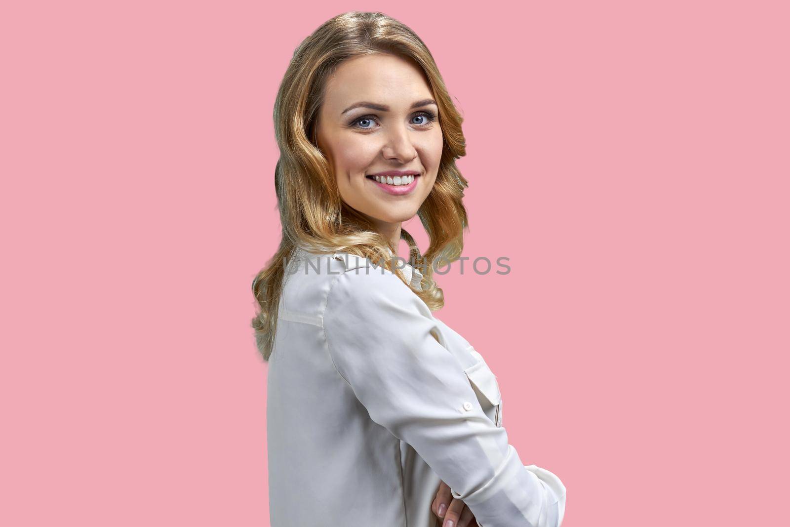 Young charming woman looking at camera with a beautiful smile. Attractive girl in white blouse posing on pink background.