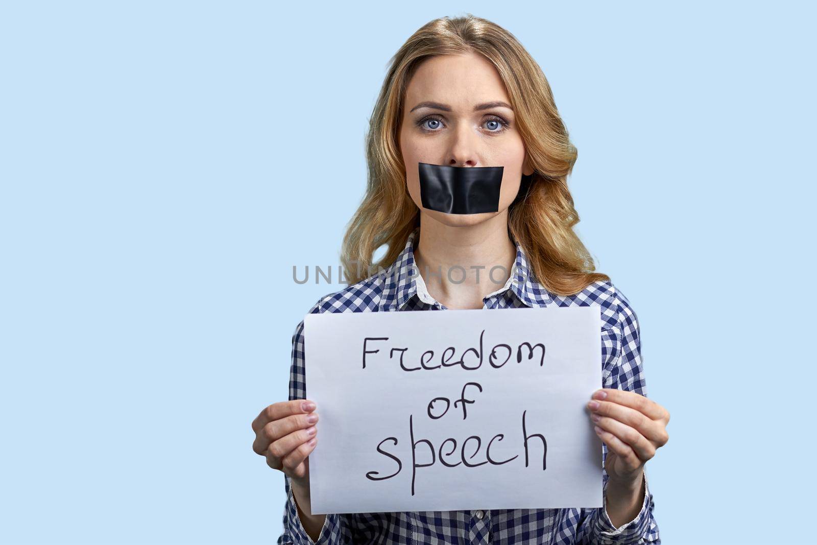 Young woman with taped mouth on blue color background. Young beautiful woman with black tape on her mouth. Freedom of speech concept.