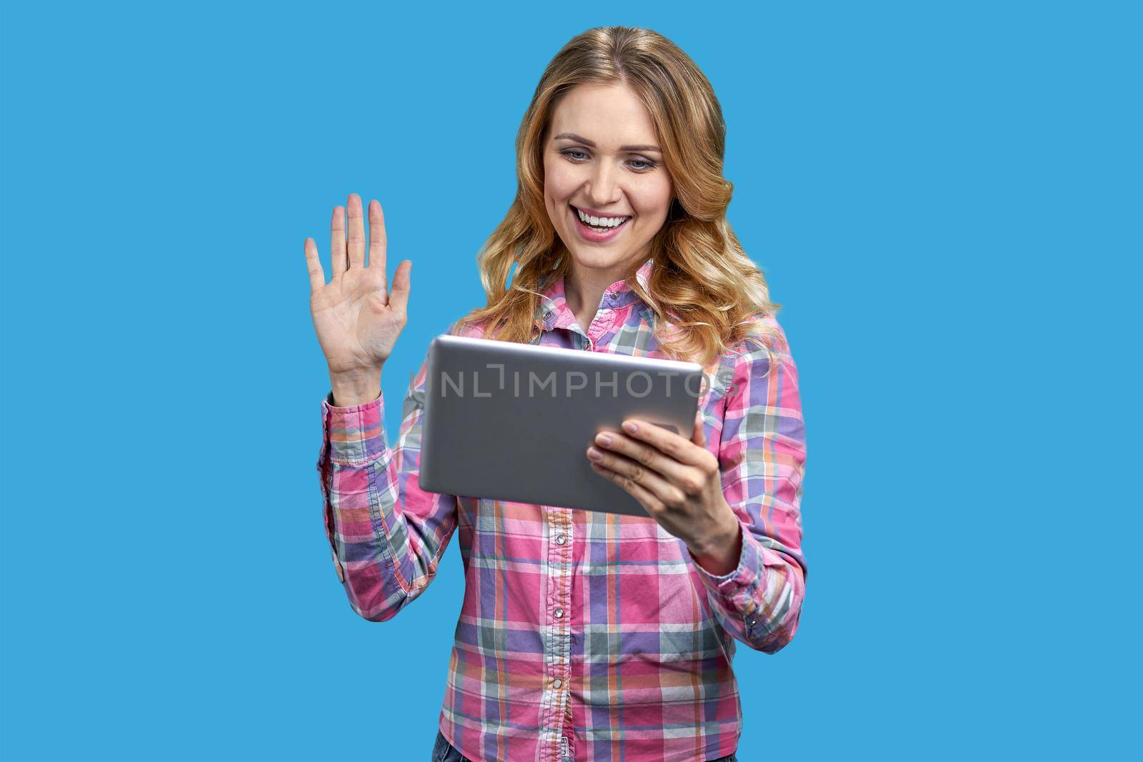 Young cheerful woman having a video call on color background. Young smiling woman holding digital tablet and waving with hand.