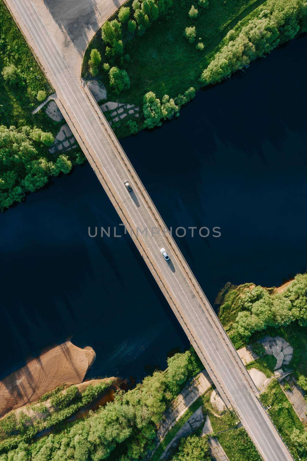 Drone top down view of empty car bridge crossing beautiful dark blue river. Aerial top view bridge in bright summer. Sunset light. Amazing drone top view vertical shot