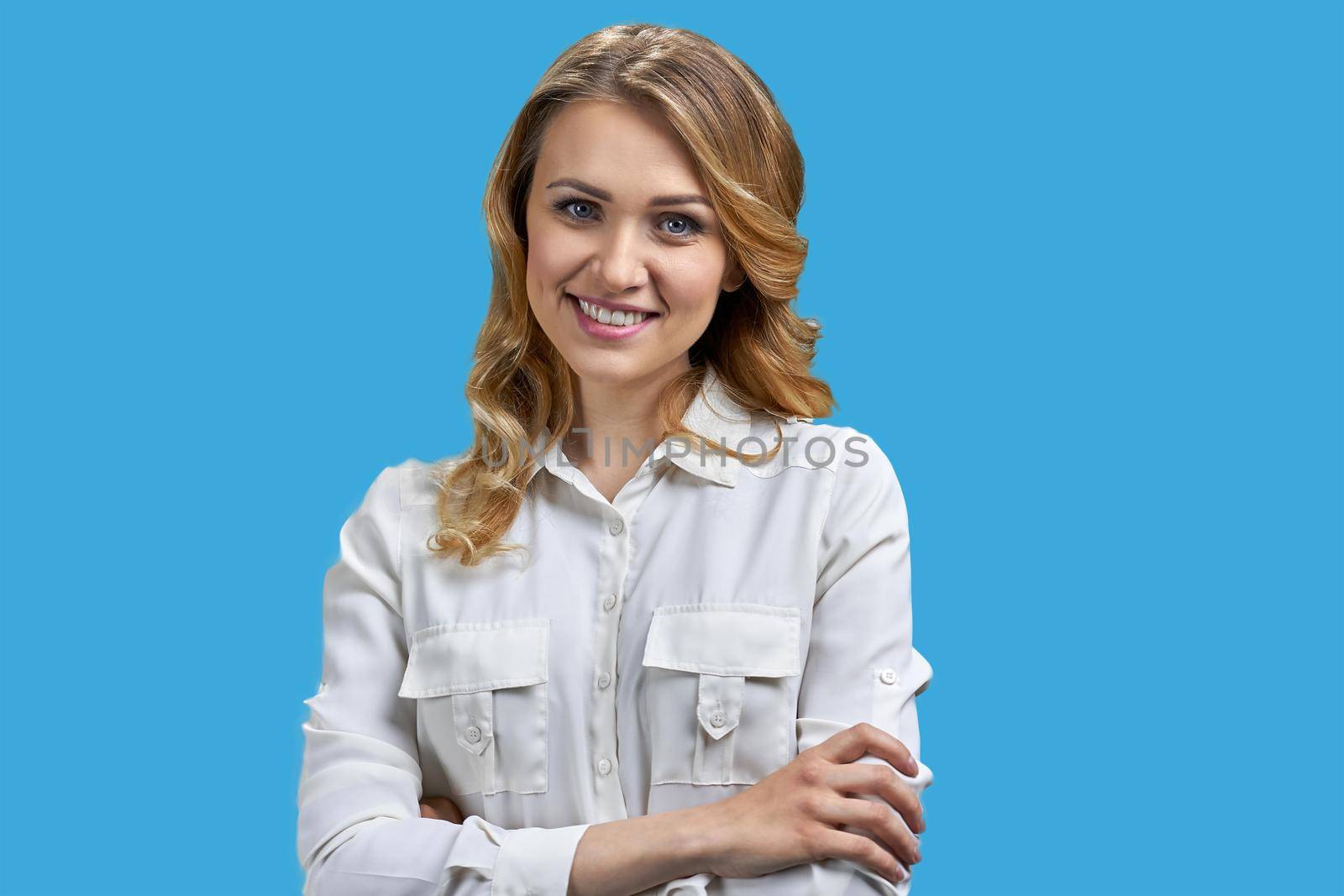 Young charming office lady posing at camera on blue background. Pretty woman in white blouse looking at camera.