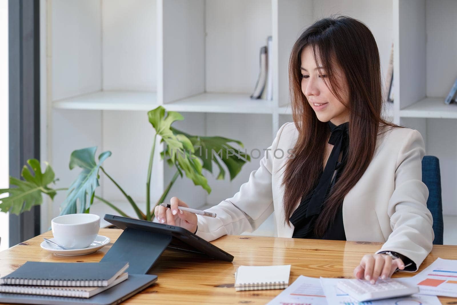 Portrait of a business woman using a tablet computer and calculator for data analysis, marketing, accounting by Manastrong