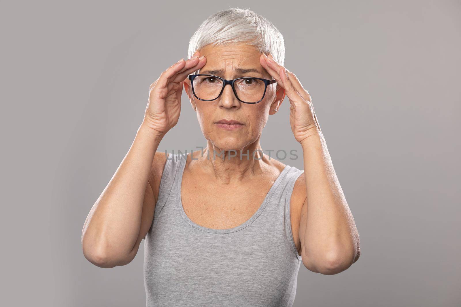 Headache. worried expression. Senior old woman with short gray hair and glasses show headache problems, healthcare and medicine concept by adamr
