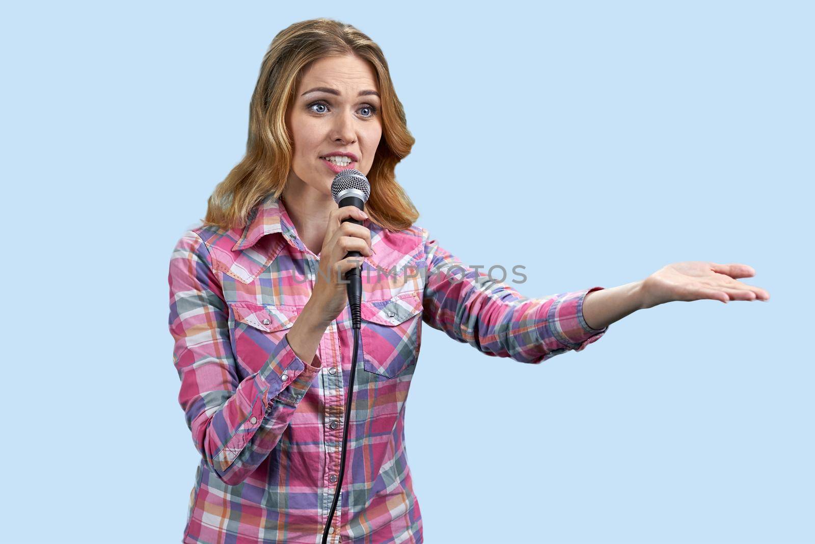 Young woman talking into microphone on color blue background. Public speaking concept.