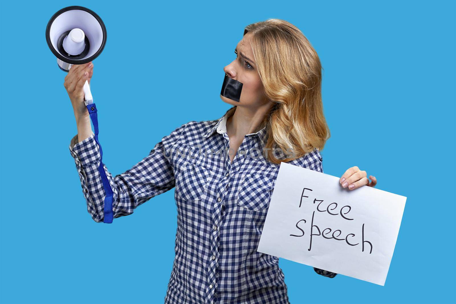 Upset woman protester with adhesive tape over mouth looking at megaphone in her hand. Free speech.