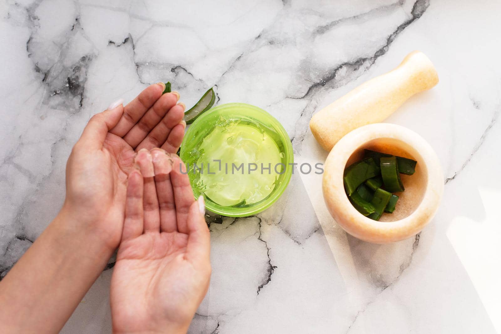 Hands of woman holding aloe gel next to mortar and chopped aloe leaf.